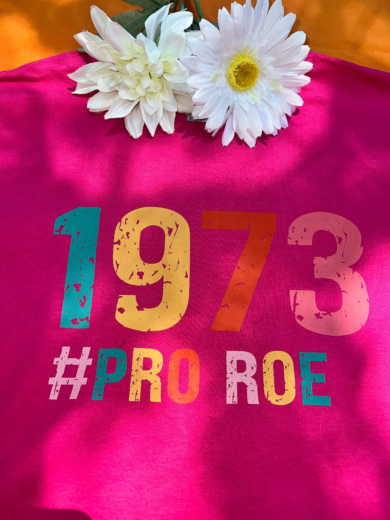 A pink t-shirt with the text '1973 PRO ROE' and some floral decorations on top.