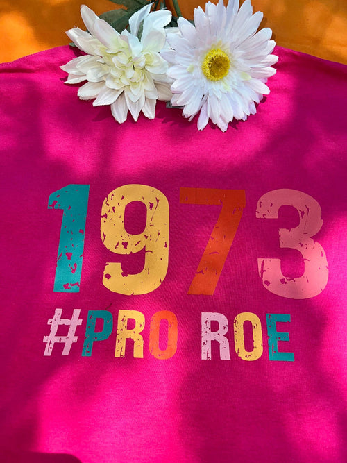 A pink t-shirt with the text '1973 PRO ROE' and some floral decorations on top.