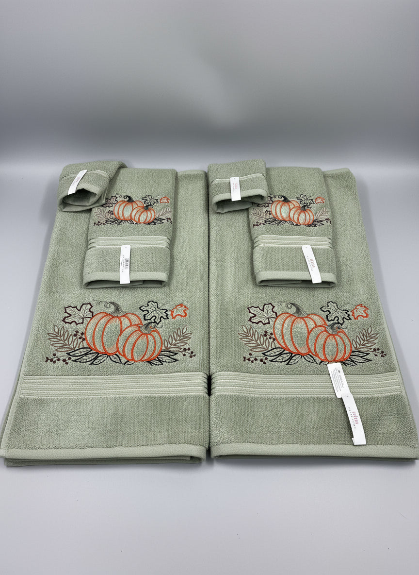 Set of green towels with embroidered pumpkins on a gray surface