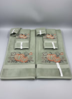 Set of green towels with embroidered pumpkins on a gray surface