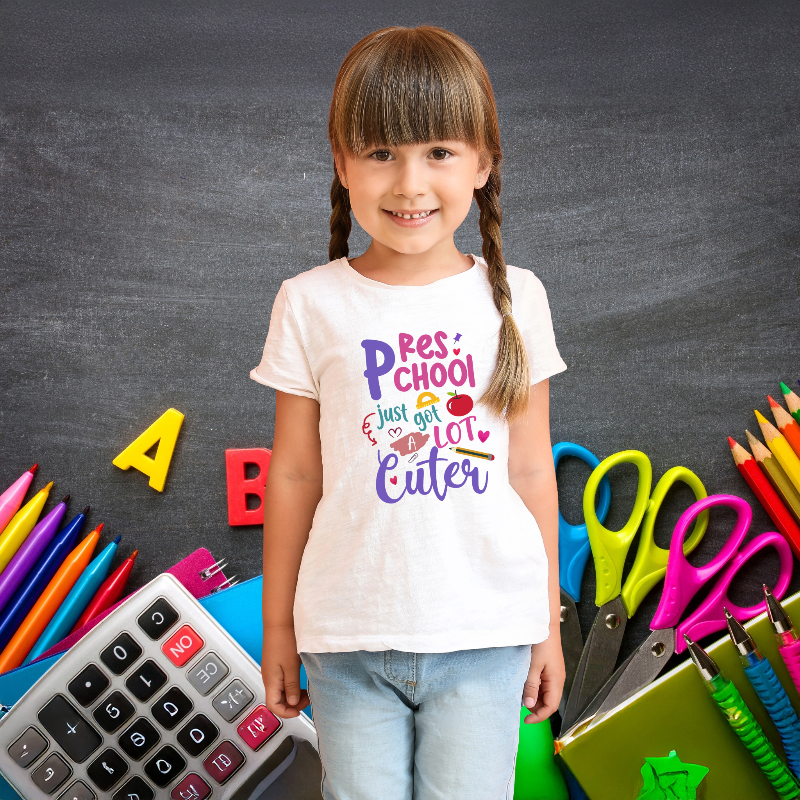 Young model wearing a white t-shirt with colorful text, standing in front of a chalkboard with educational supplies.