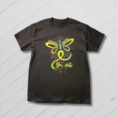 Black t-shirt with a green butterfly design on a wooden surface with a yellow flower field background