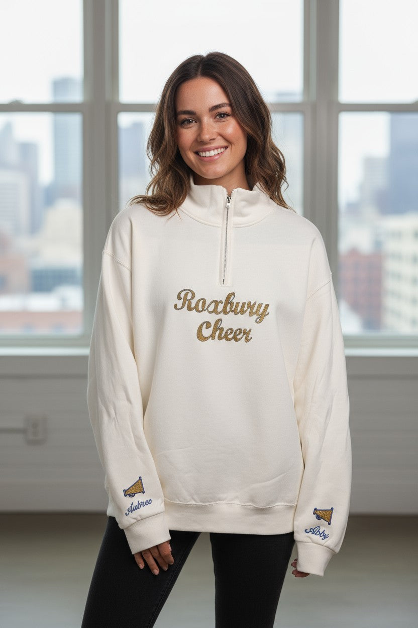 Woman wearing a white sweatshirt with 'Roarway Cheer' text, standing in front of a window with a cityscape view.
