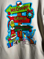 Close up of a cream-colored t-shirt with a graphic design featuring the character 'The Grinch' and a whimsical road sign pointing to Mt. Crumpit and Whoville.