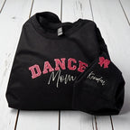 Black sweatshirt with 'DANCE Mom' text and a bow design on a wooden surface