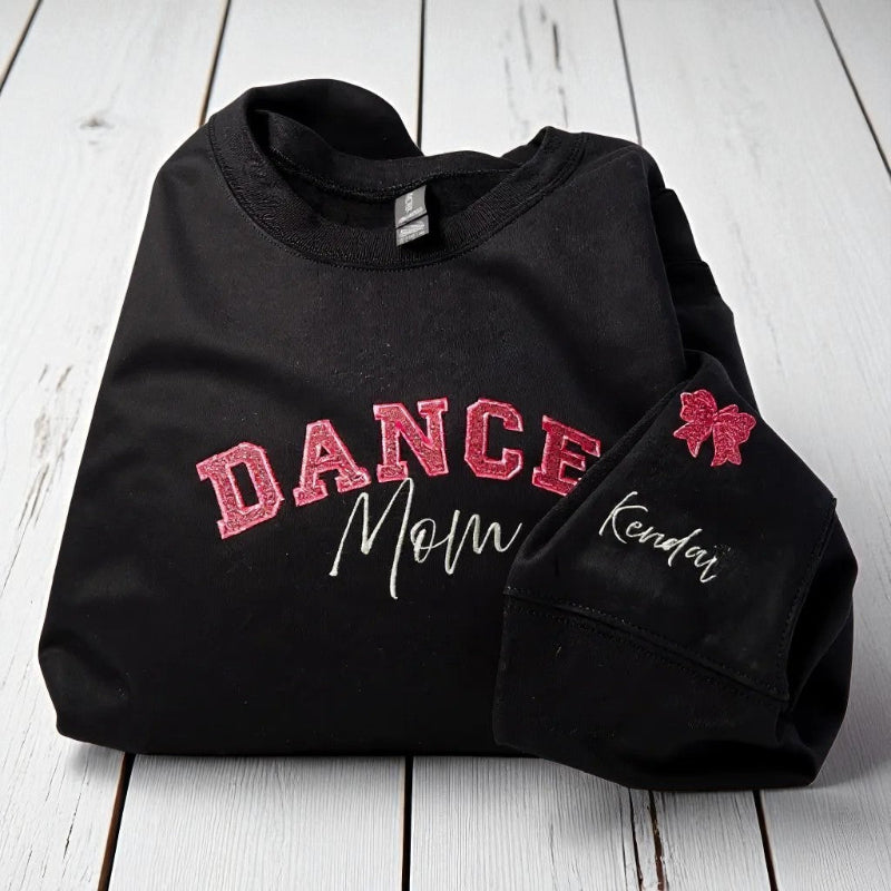 Black sweatshirt with 'DANCE Mom' text and a bow design on a wooden surface