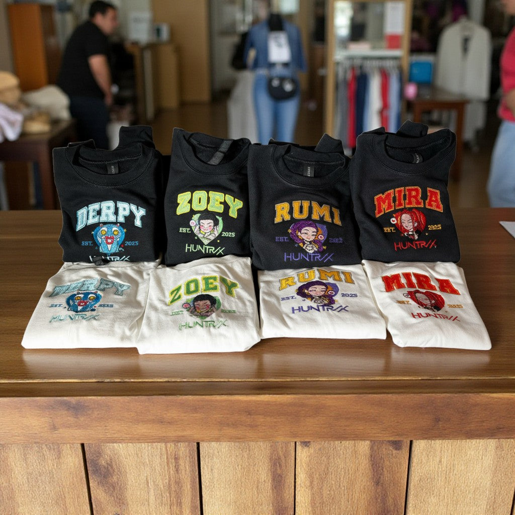 Collection of black and white t-shirts with colorful text and graphics on a wooden surface.