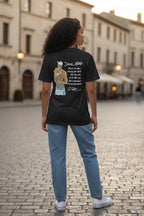 Person wearing a black t-shirt with a graphic design on the back, standing on a cobblestone street.