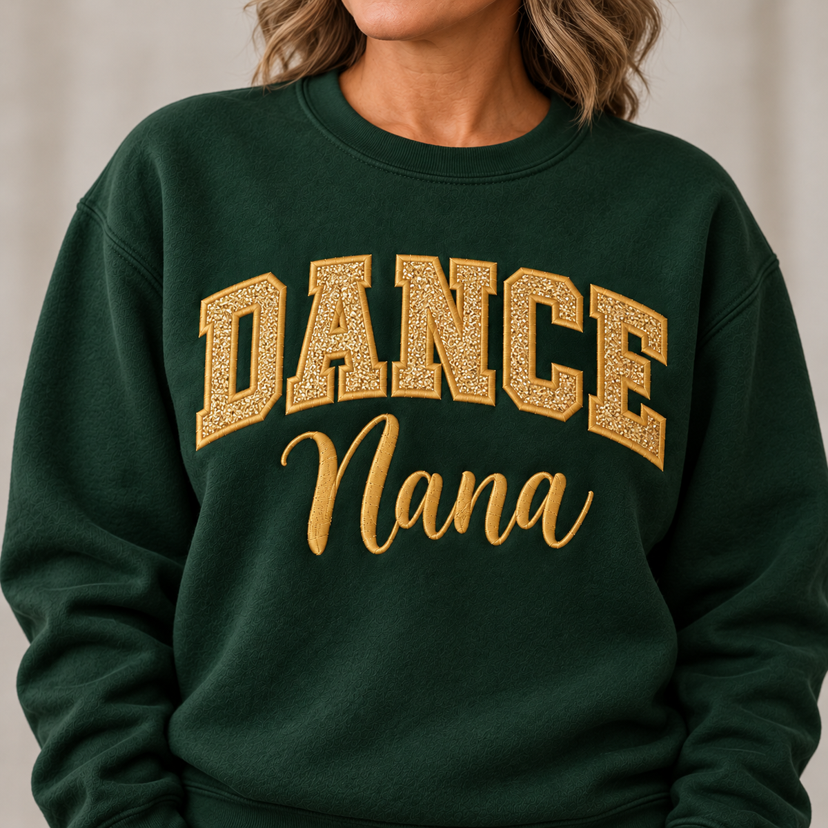 A close-up of a person wearing a dark green crewneck sweatshirt with 'DANCE Nana' printed in gold lettering across the chest.