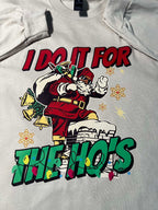 A cream-colored t-shirt with a graphic print of Santa Claus and the text 'I Do It for the Ho's' surrounded by Christmas lights.