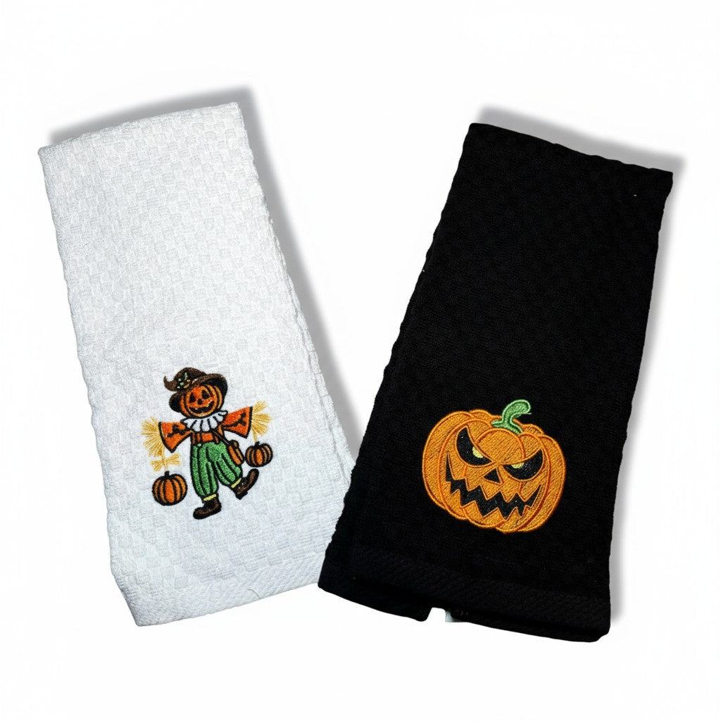 Two Halloween-themed kitchen towels, one white with a scarecrow and one black with a jack-o'-lantern, on a white background.