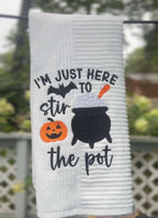 Halloween towel embroidered with a cauldron, pumpkin, bat, and the words “I’m Just Here to Stir the Pot.”