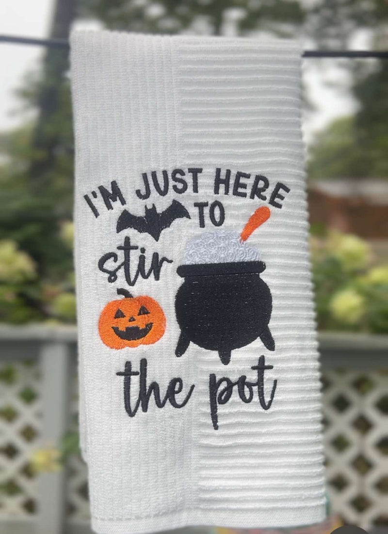 Halloween towel embroidered with a cauldron, pumpkin, bat, and the words “I’m Just Here to Stir the Pot.”