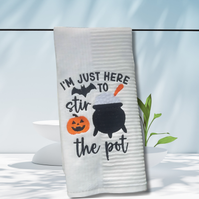 Halloween towel embroidered with a cauldron, pumpkin, bat, and the words “I’m Just Here to Stir the Pot.”