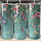 A set of three stainless steel tumblers with a floral design, featuring pink and white flowers and green leaves on a blue background, displayed on a wooden surface.