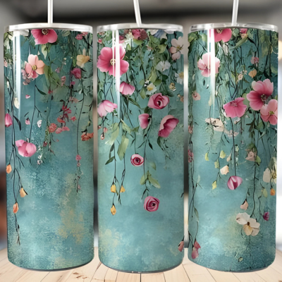 A set of three stainless steel tumblers with a floral design, featuring pink and white flowers and green leaves on a blue background, displayed on a wooden surface.