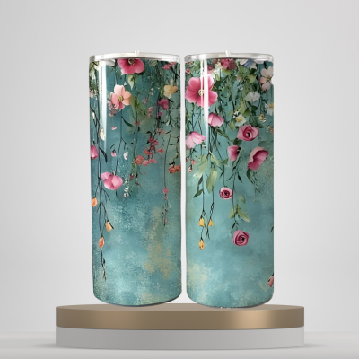 A set of three stainless steel tumblers with a floral design, featuring pink and white flowers and green leaves on a blue background, displayed on a wooden surface.