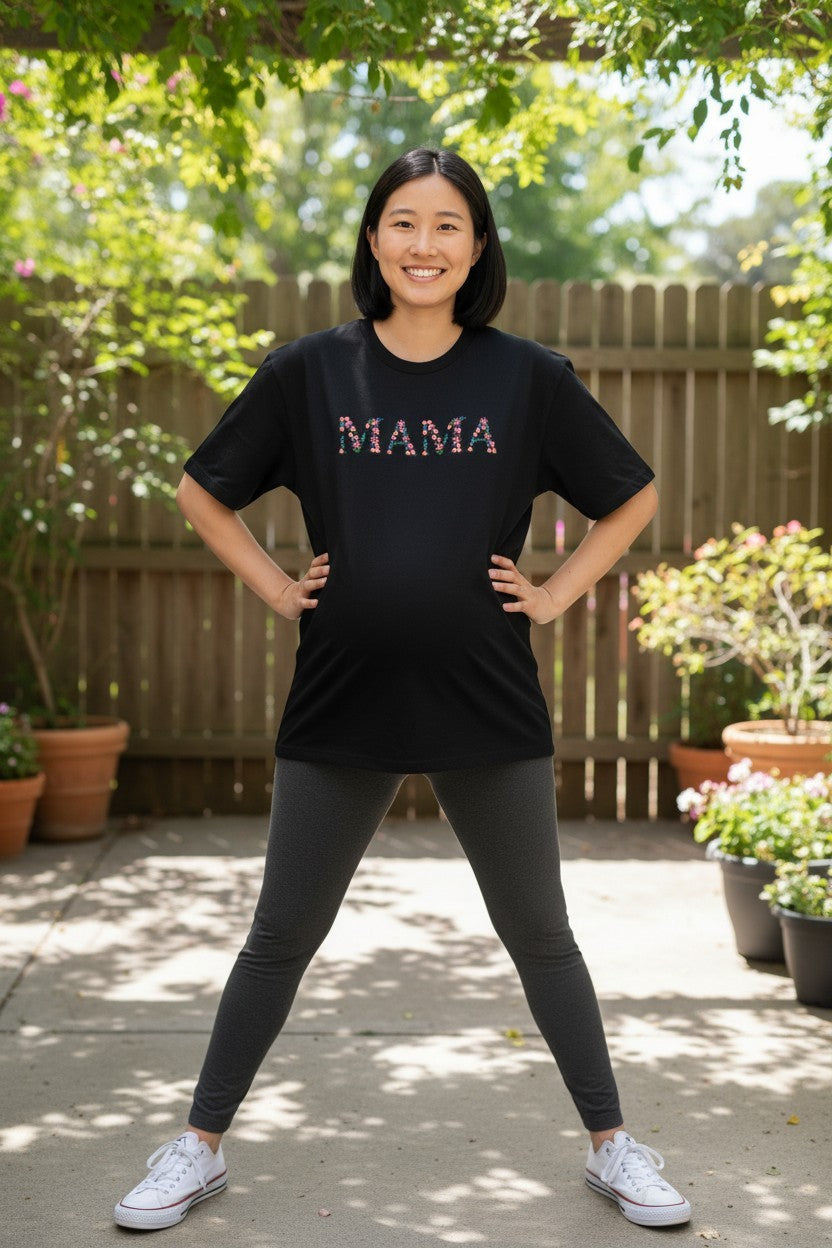 Woman wearing a black t-shirt with 'MAMA' on it in an outdoor setting.