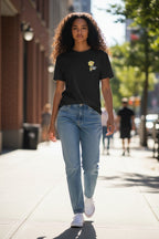Person wearing a black t-shirt with a yellow graphic and light blue jeans walking on a city street.