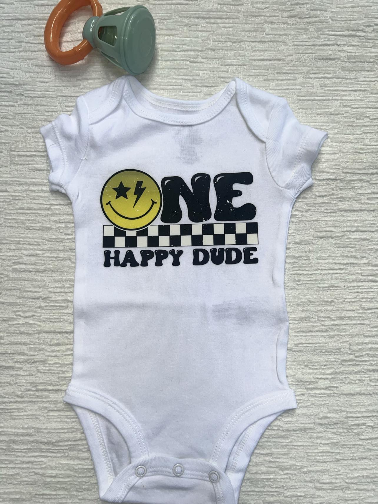 A white baby onesie with the words: "One Happy Dude"
