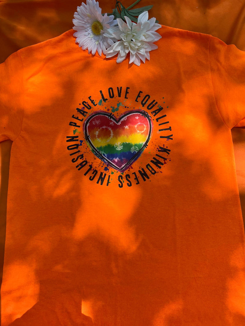 An orange t-shirt with a graphic design supporting LGBTQ+ pride, featuring a heart shape made from different colored arrows forming a rainbow, and the text 'Love is Love'.