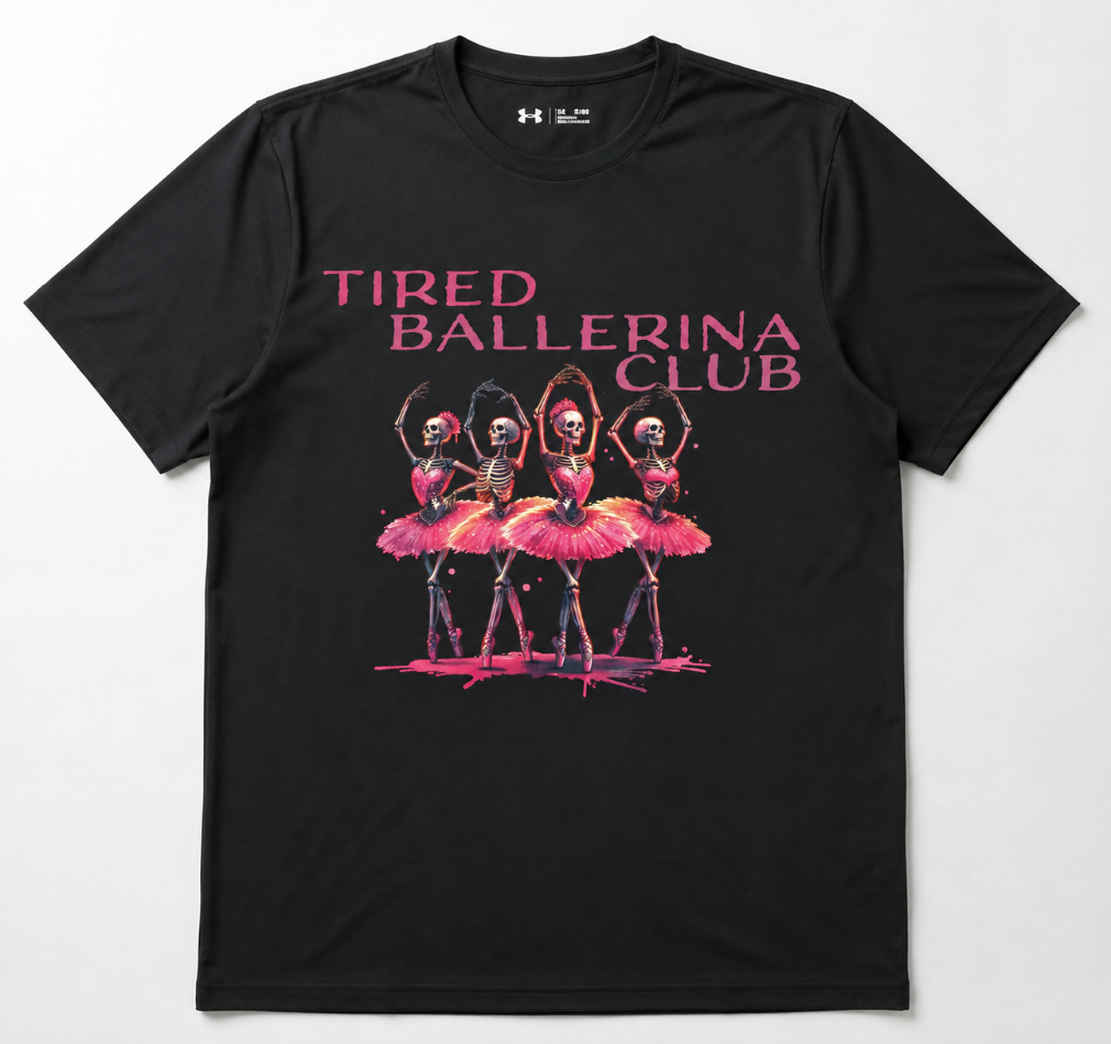 A black short-sleeve t-shirt with a graphic print of four ballerinas in pink tutus under the text 'TIRED BALLERINA CLUB' in pink, on a light gray background.