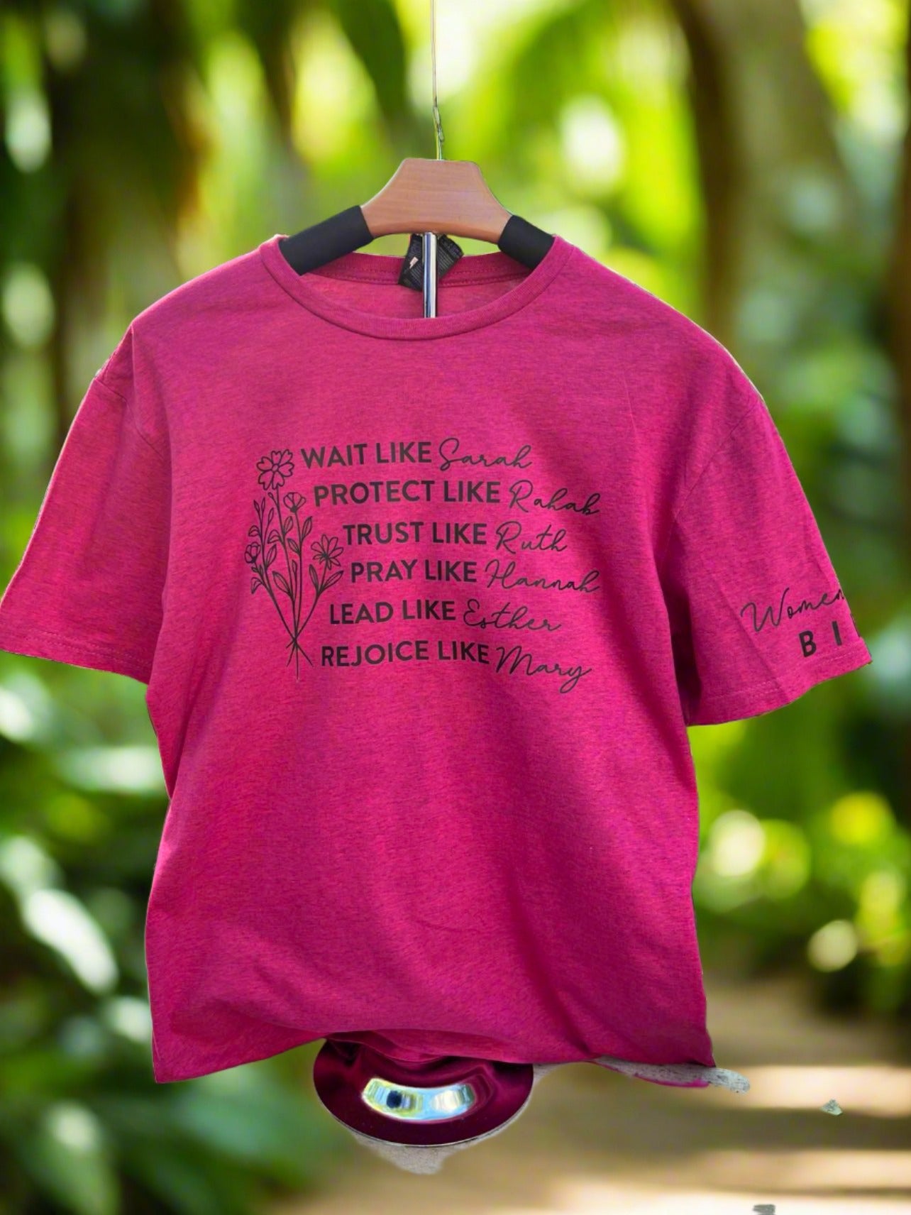 Berry colored tee shirt with strong woman of the bible listed on the front of the shirt.  An additional image is on the left sleeve of the shirt.