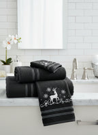 Set of black towels with white deer and snowflake designs on bathroom sink surface.