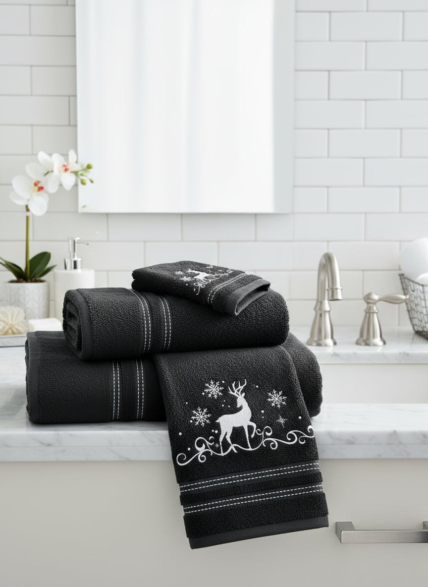 Set of black towels with white deer and snowflake designs on bathroom sink surface.