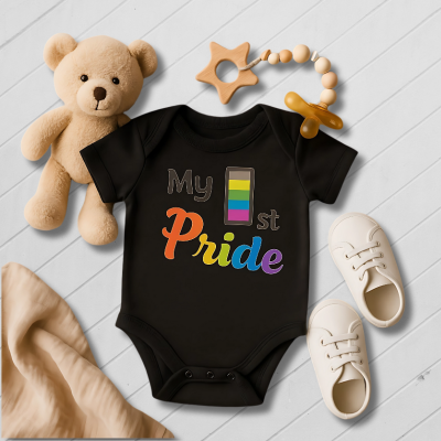 Black baby onesie with 'My 1st Pride' text, surrounded by toys on a light wooden floor.