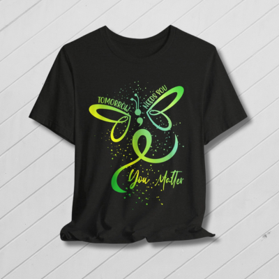 Black t-shirt with a green butterfly design on a wooden surface with a yellow flower field background