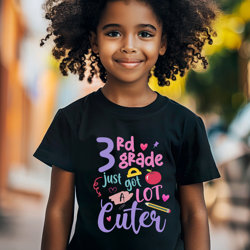 Child wearing a black t-shirt with colorful text and graphics, standing outdoors.