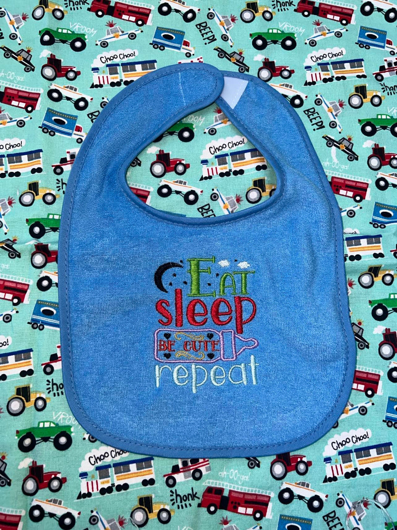 Blue baby bib with an embroidery design that says: Eat, Sleep, Be Cute, Repeat"