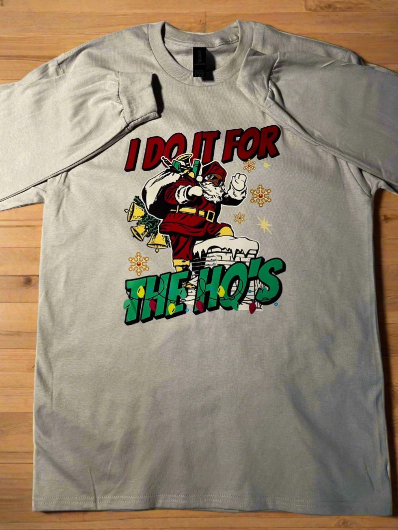 A cream-colored t-shirt with a graphic print of Santa Claus and the text 'I Do It for the Ho's' surrounded by Christmas lights.