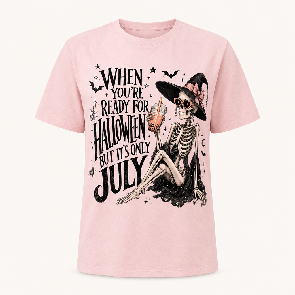 A light pink short-sleeve t-shirt with a graphic print of a skeleton witch holding an orange drink, next to the text 'WHEN YOU'RE READY FOR HALLOWEEN BUT IT'S ONLY JULY'.