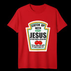 A red short-sleeve crewneck t-shirt with a parody graphic designed to look like a ketchup bottle label. The graphic reads 'CATCH UP WITH JESUS LETTUCE PRAISE & RELISH HIM' with two small tomatoes and a quote at the bottom, set against a solid black background.
