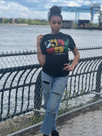 A person standing by a fence wearing a graphic t-shirt with Juneteenth-themed design featuring an African American woman with a powerful afro and graffiti-style artwork.