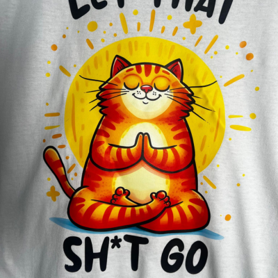 Close-up of orange yoga cat graphic with “Let That Sht Go” text on soft cotton tee