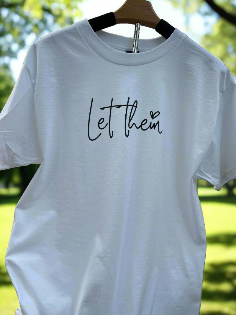 White t-shirt with “Let Them” message in script font and small heart on the front, inspirational faith-based tee for women.