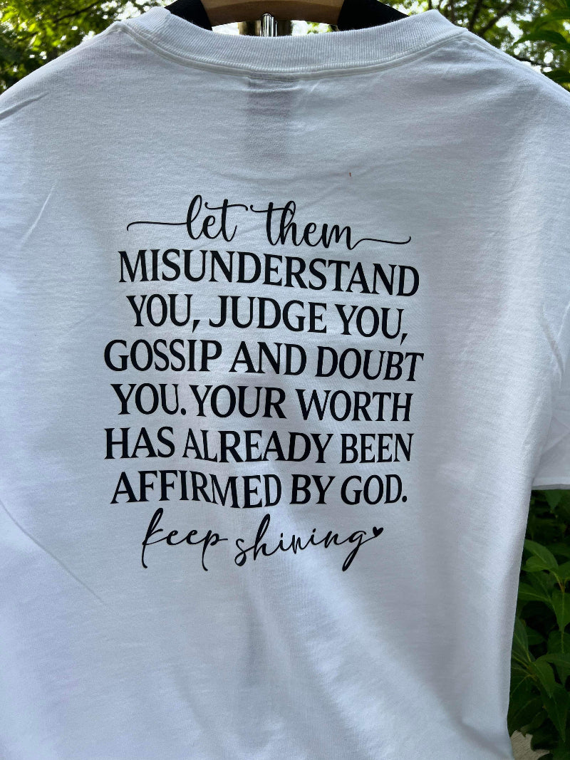 Back of white t-shirt with motivational quote: “Let them misunderstand you, judge you, gossip and doubt you. Your worth has already been affirmed by God. Keep shining.”