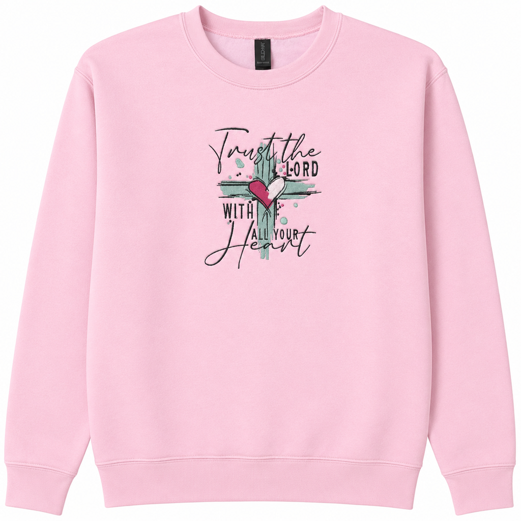 A light pink crewneck sweatshirt featuring a embroidered design  the chest with a teal cross, a red heart, and the text 'Trust the LORD with all your heart' in black script and block lettering.
