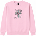 A light pink crewneck sweatshirt featuring a embroidered design  the chest with a teal cross, a red heart, and the text 'Trust the LORD with all your heart' in black script and block lettering.