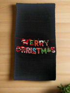 Black kitchen towel with colorful embroidered "Merry Christmas" letters on a string