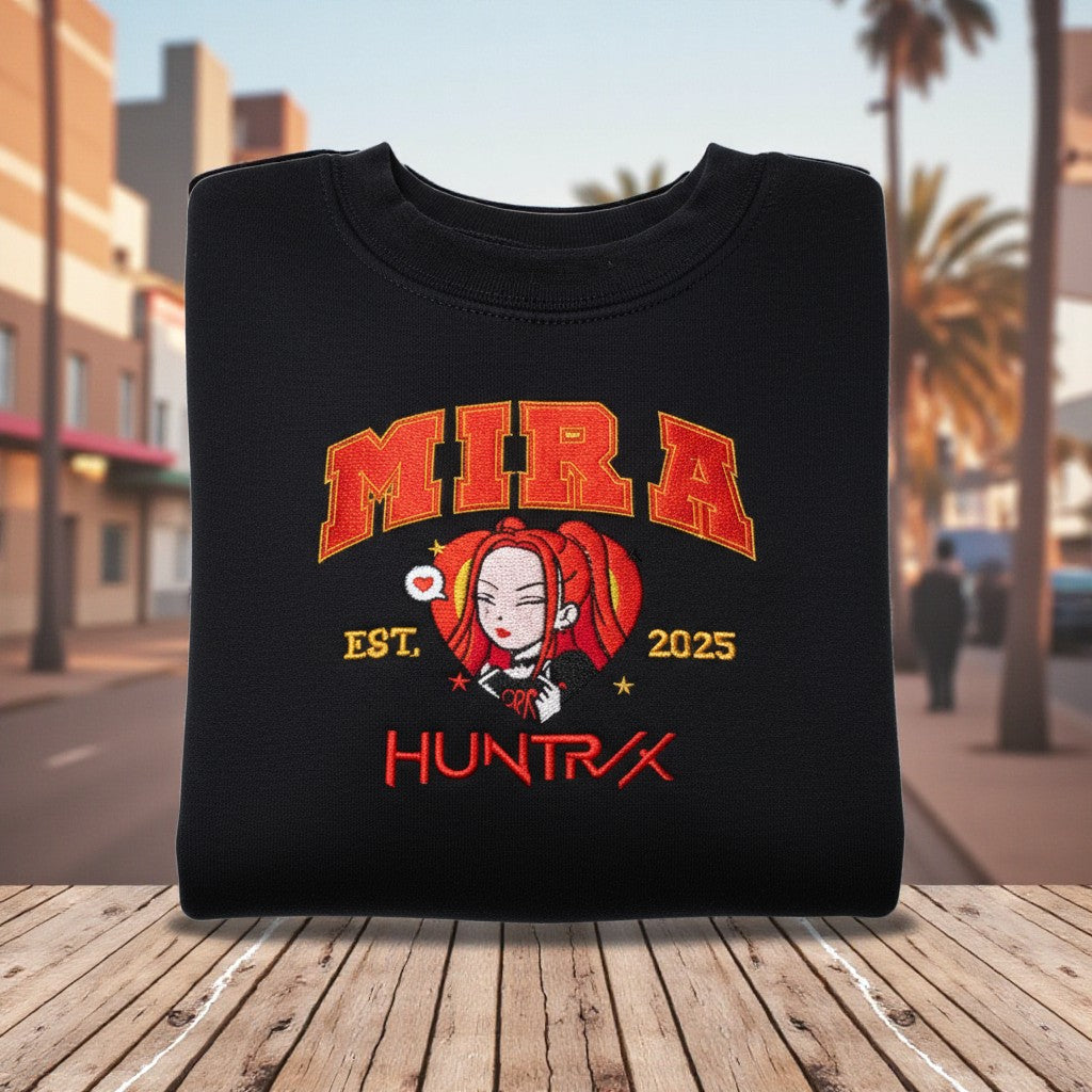 Black sweatshirt with 'MIRA HUNTRX' design on a wooden surface with a cityscape background