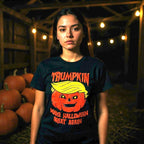 Woman wearing Trumpkin Halloween shirt with pumpkin design and “Make Halloween Great Again” text, standing in barn with pumpkins.