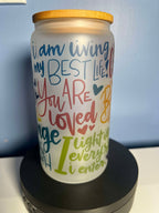 A frosted glass motivational cup with colorful text and designs, displaying affirmations such as 'You are worthy of love' and 'You are loved', with a bamboo lid on top and a straw included.
