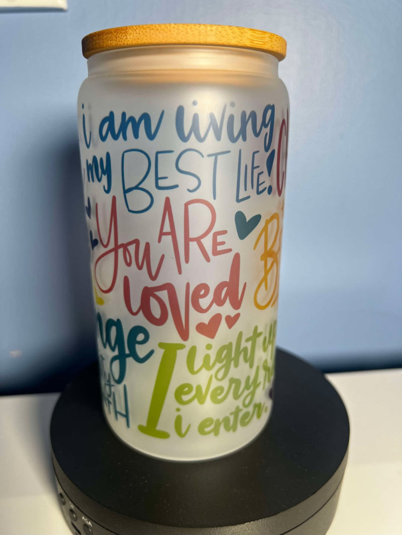 A frosted glass motivational cup with colorful text and designs, displaying affirmations such as 'You are worthy of love' and 'You are loved', with a bamboo lid on top and a straw included.