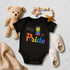 Black baby onesie with 'My 1st Pride' text, surrounded by toys on a light wooden floor.