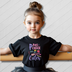 Child wearing a black t-shirt with colorful text on a white wooden floor.