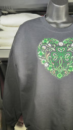 Black crewneck sweatshirt featuring intricate green Celtic clover heart design with floral detailing